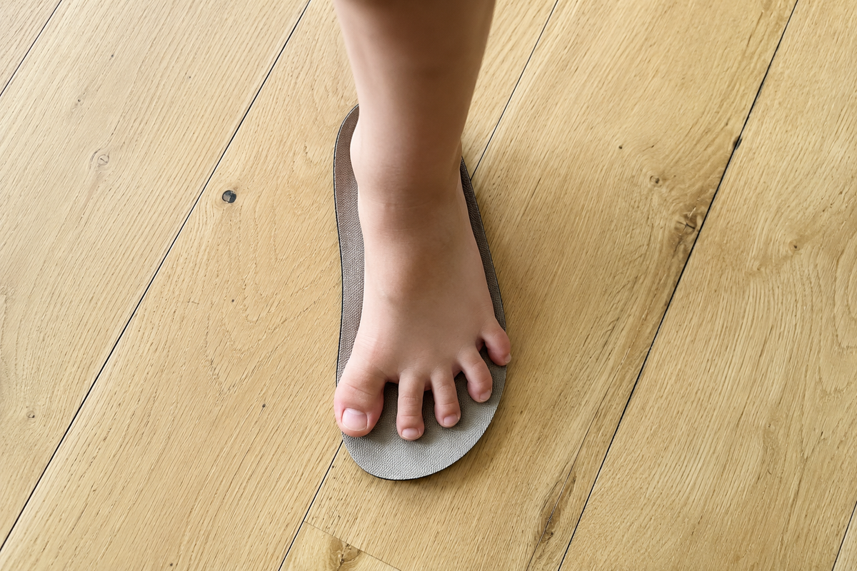 A child standing barefoot on the insole of their shoe